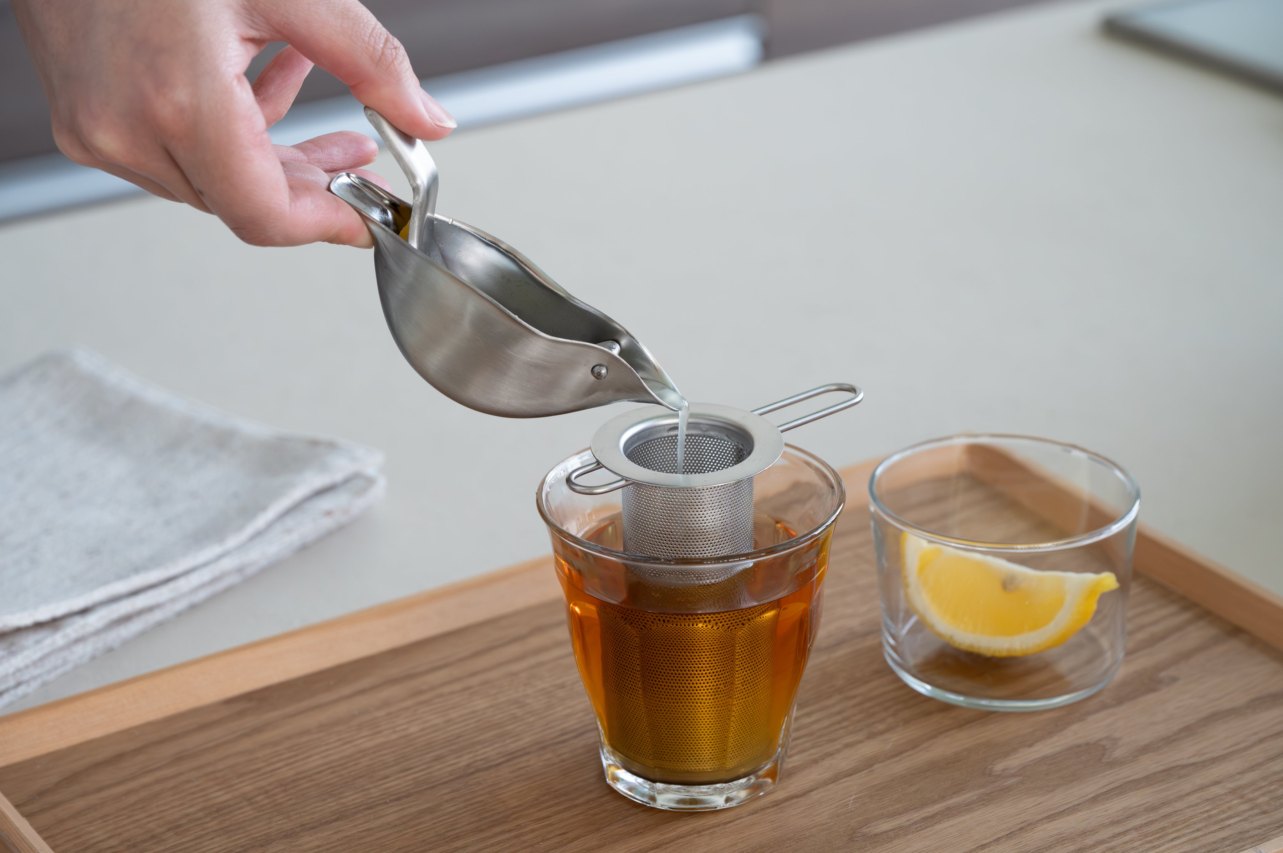 KAJIdonya bird-shaped citrus squeezer pouring juice through a stainless steel strainer into a glass.