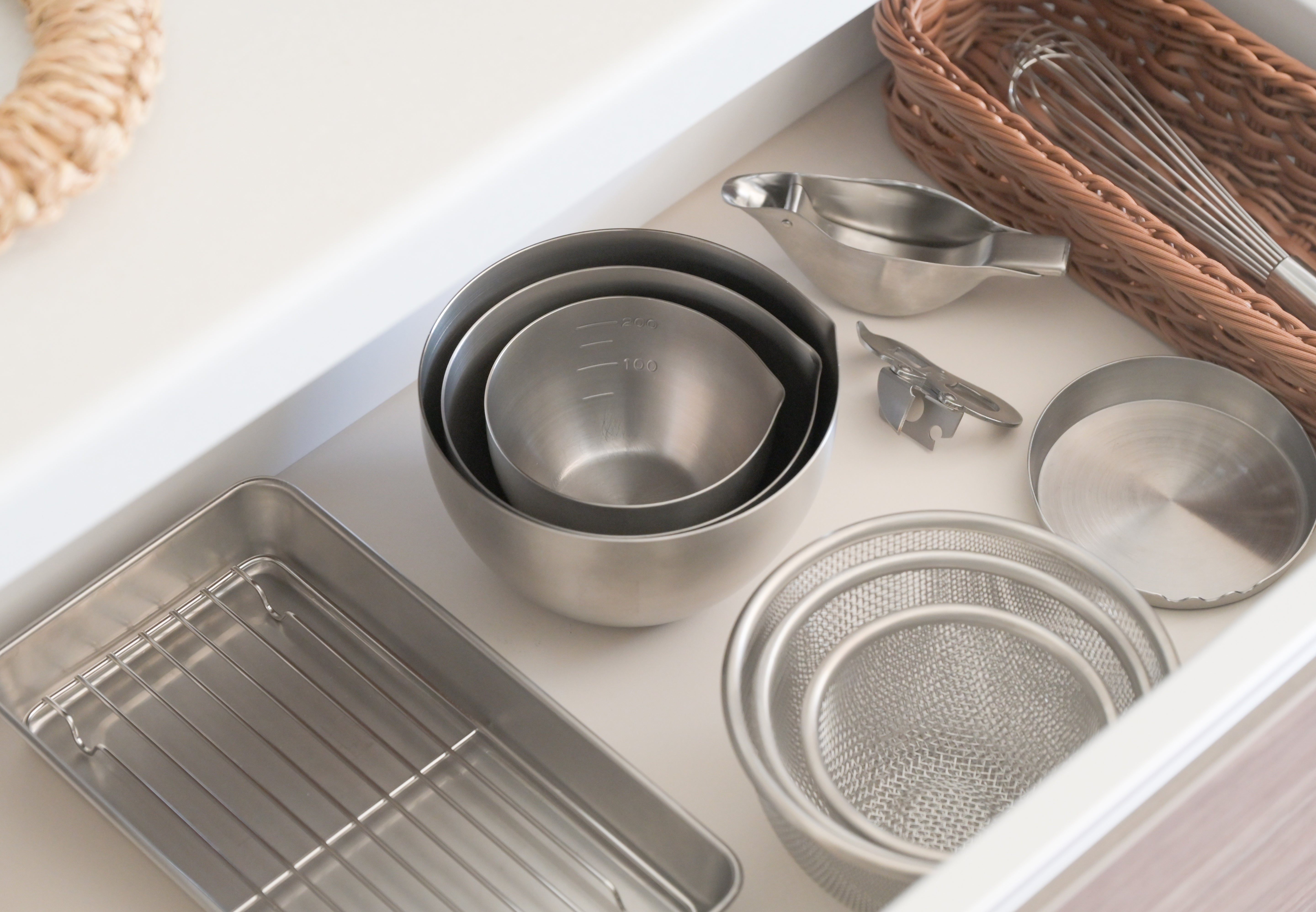 KAJIdonya stainless steel kitchen tools organised in a drawer, including bowls, strainers and trays.