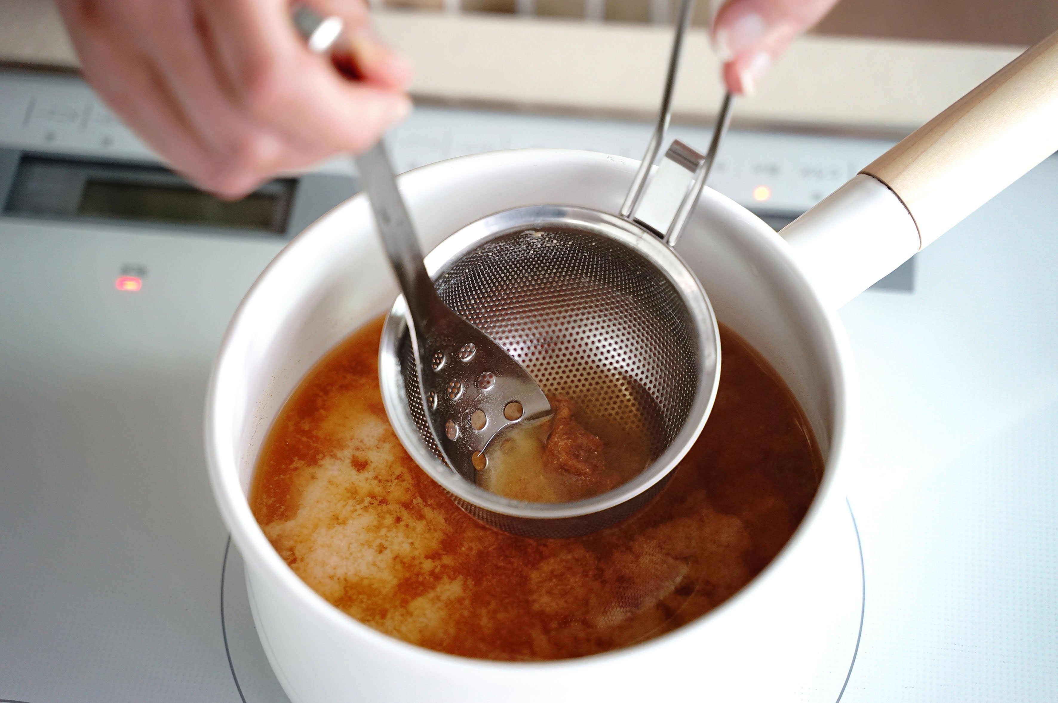 KAJIdonya punched miso strainer and spoon being used to dissolve miso in a saucepan.