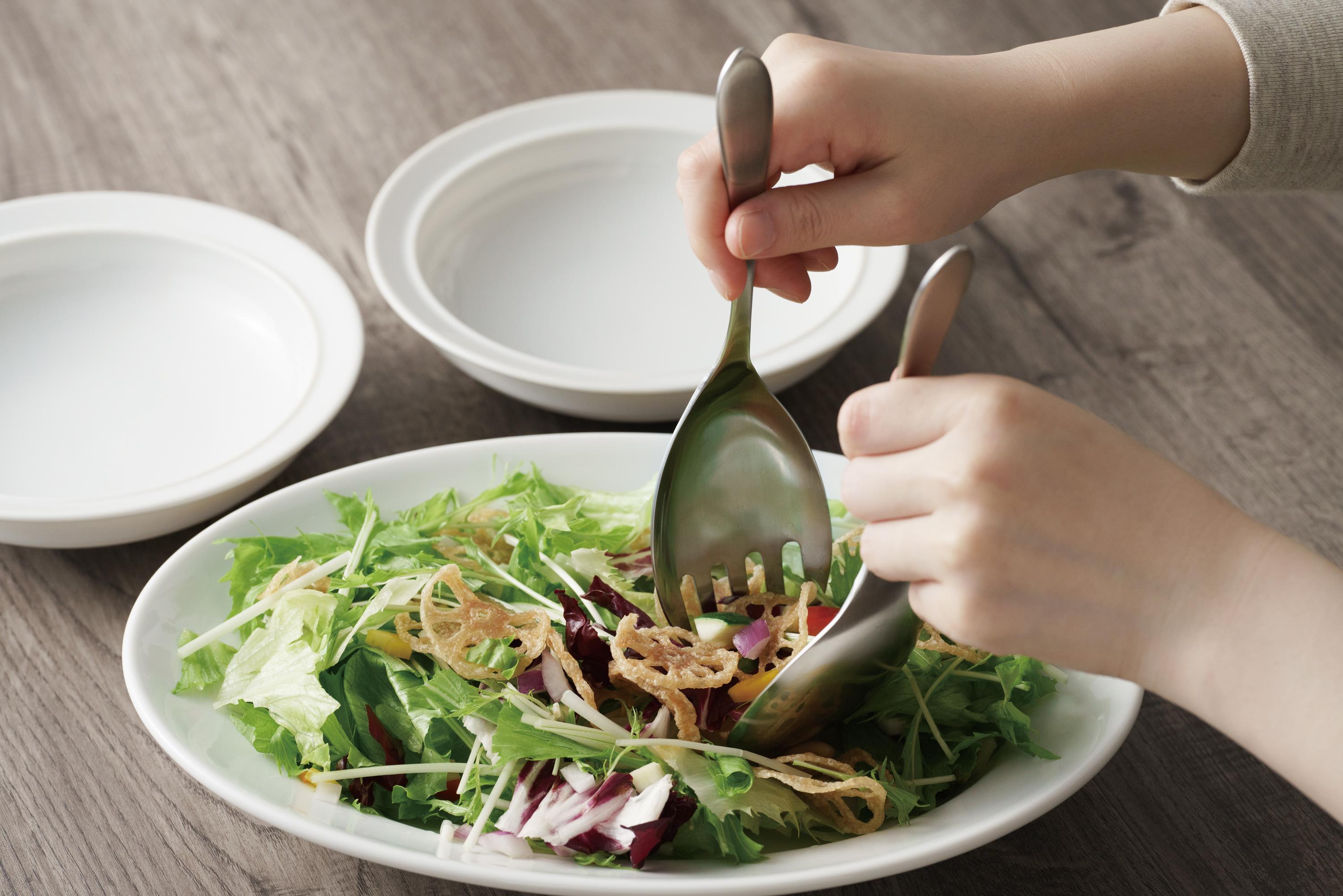 KAJIdonya stainless steel serving utensils being used to toss a fresh salad.